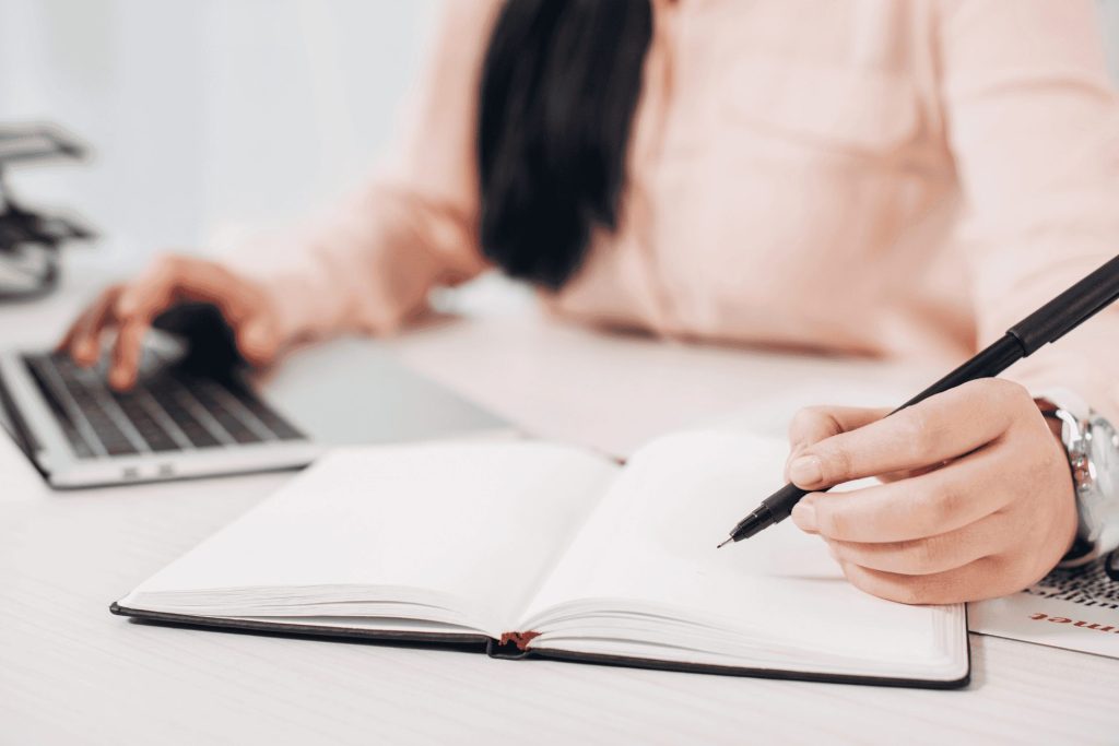 Woman using a laptop and writing in a notebook