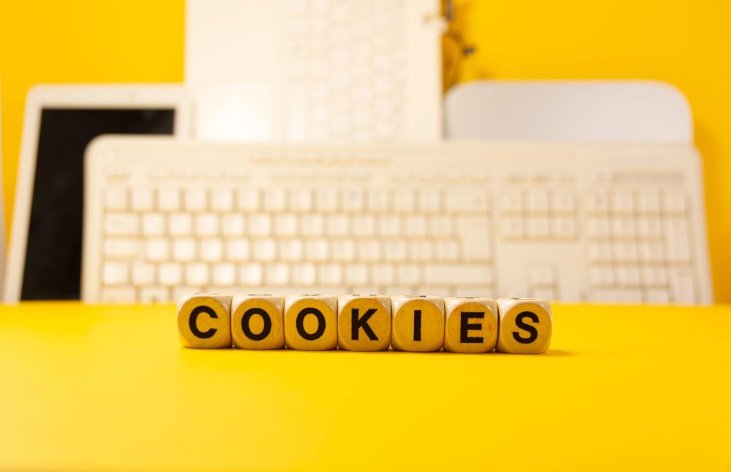 Blurred yellow background with keyboards and wooden blocks in focus that spell out ‘cookies’
