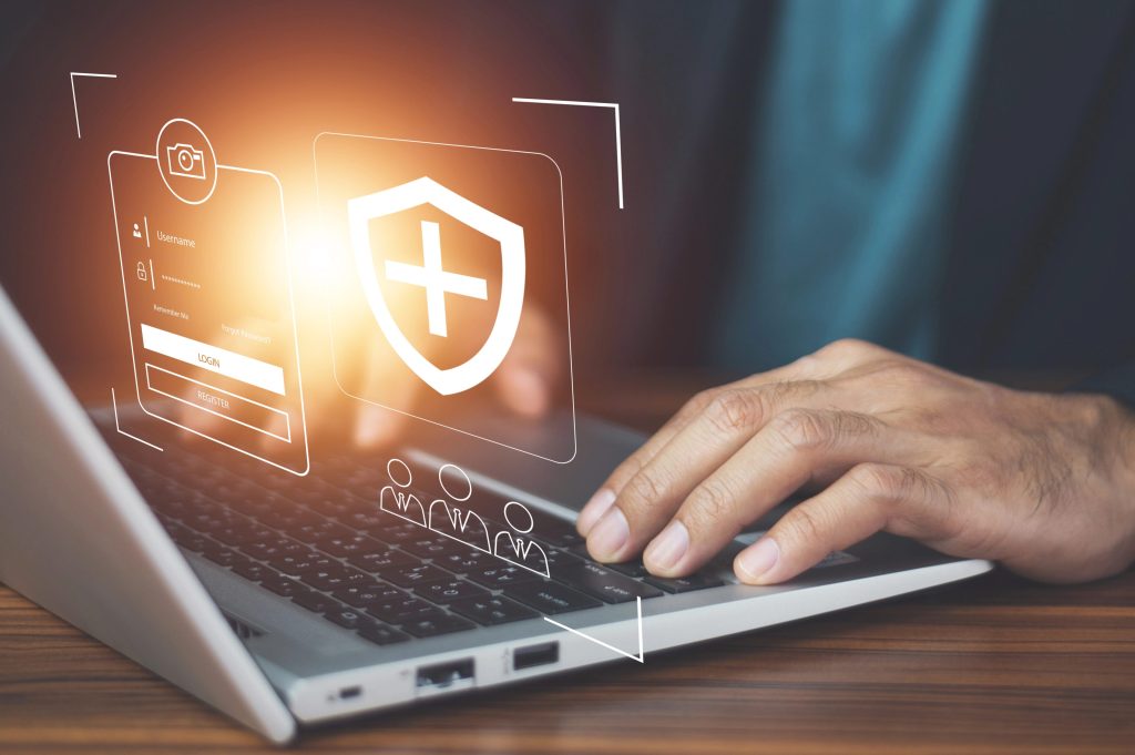 A hand on a laptop keyboard, with a graphic of a shield popping out of the screen