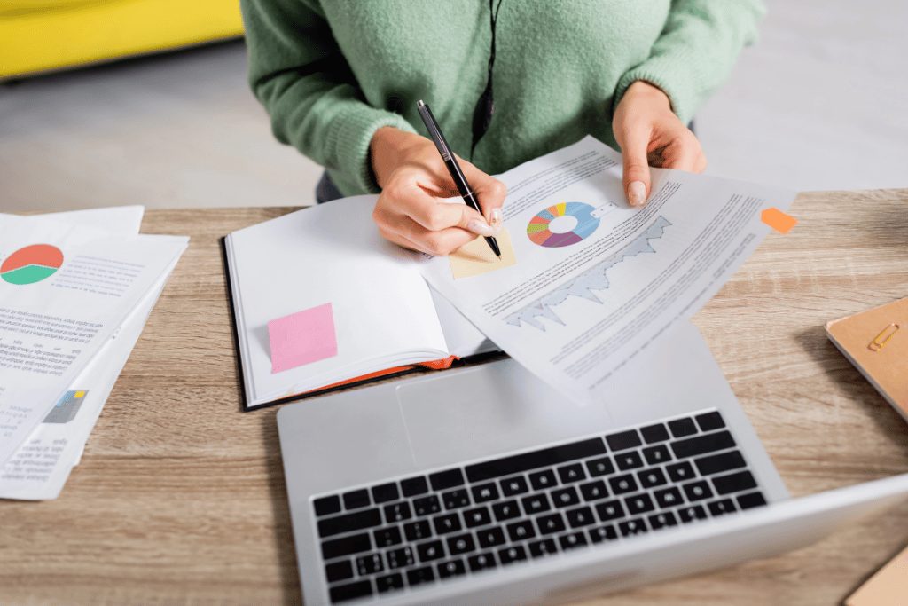 person looking at charts on paper, next to a laptop