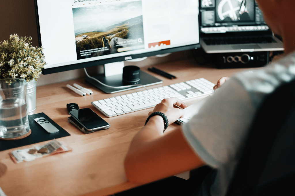 Person sat at a computer desk with a monitor showing a website design